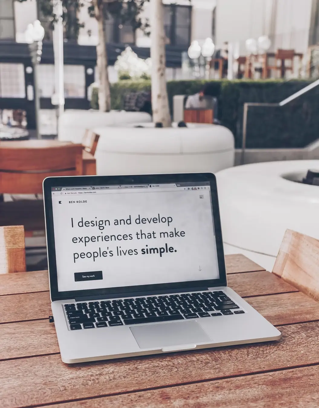 A laptop sitting on a table showing a site with the text 'I design and develop experiences that make people's lives simple'.