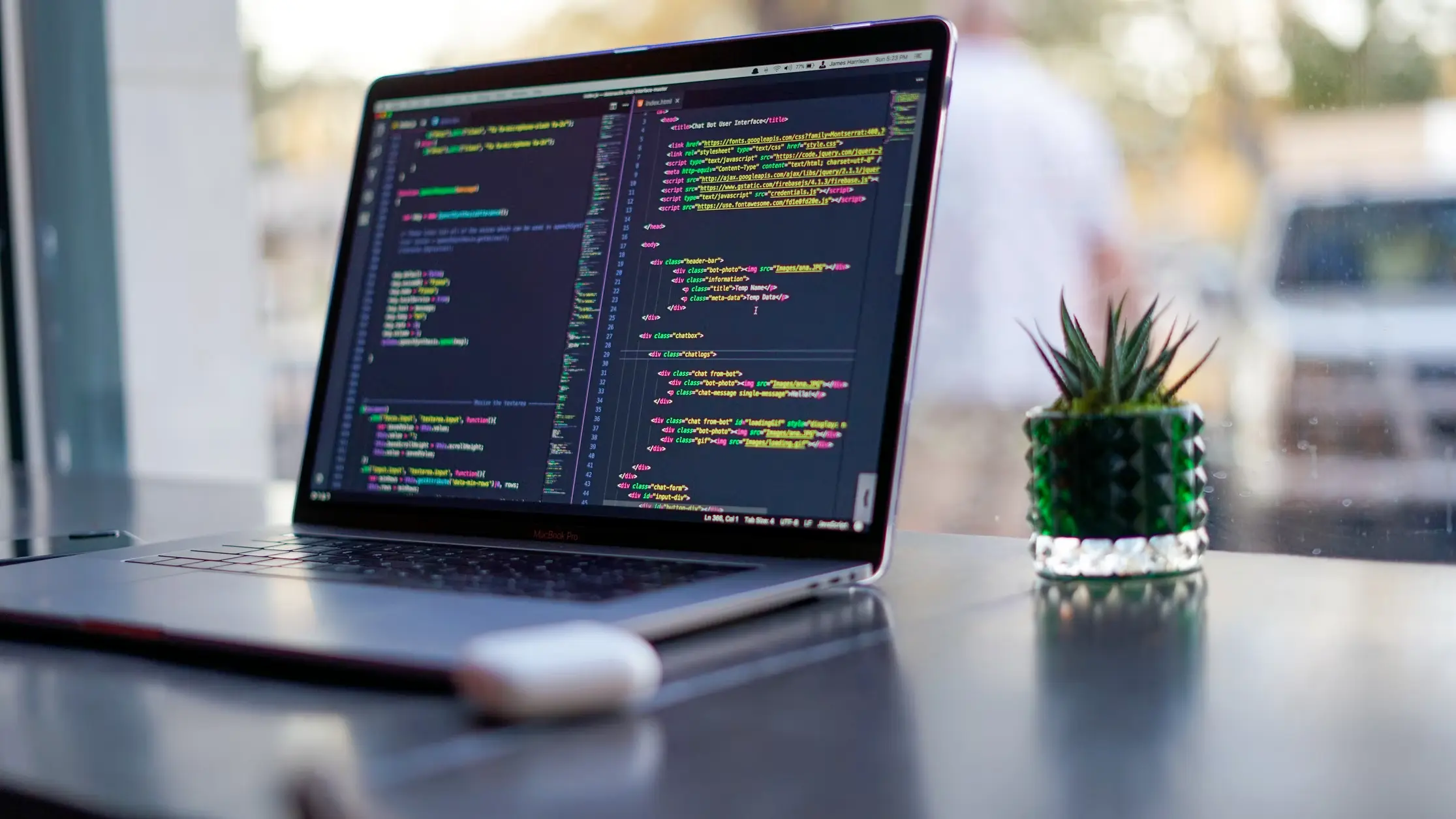 A MacBook Pro displaying HTML code on a desk next to a small green succulent plant in a textured glass pot.